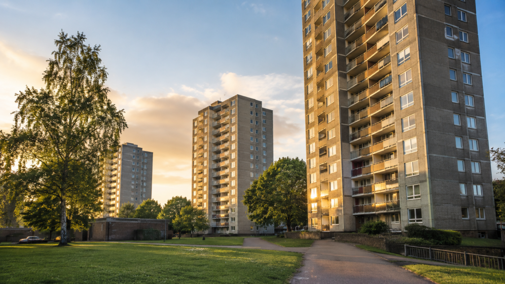 Post-war council tower blocks on a UK estate at golden hour, with green space, trees and residential pathways.