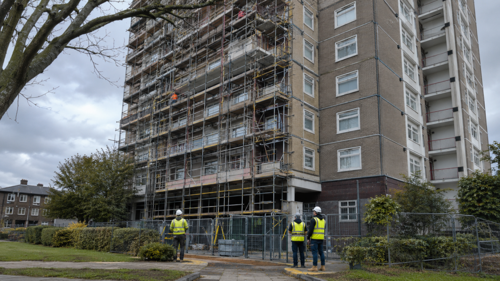 Residential high-rise building undergoing planned remediation works with scaffolding and workers in PPE.